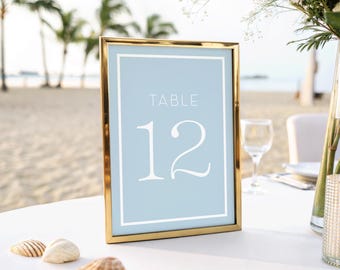 May include: A gold-framed table number sign with a light blue background and white text. The sign reads "TABLE 12".