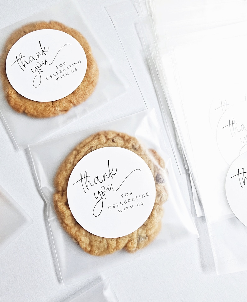 May include: Two clear plastic bags containing cookies. Each cookie has a white round sticker with black text that reads "Thank you for celebrating with us".