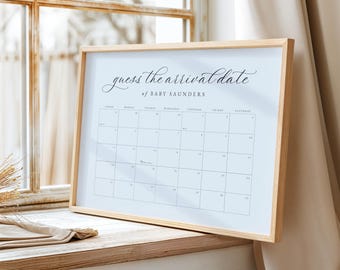 May include: A framed calendar with the text "guess the arrival date of BABY SAUNDERS" in elegant script. The calendar grid is printed in black on a white background, with a light wood frame. The calendar is displayed on a wooden surface.