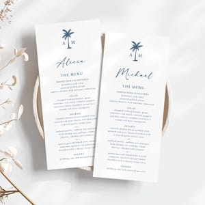 May include: Two white wedding menu cards featuring blue palm tree illustrations and the names Alicia and Michael. The menu includes passed hors d'oeuvres, salad, entrees, and dessert.
