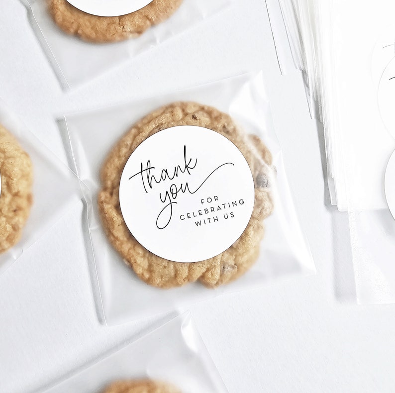 May include: A clear plastic bag containing a round, brown cookie. The cookie has a white circular sticker with the text "Thank you for celebrating with us".
