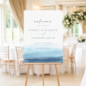 Może przedstawiać: Tablica powitalna na ślub z akwarelowym tłem w odcieniach niebieskiego. Na tablicy widnieje napis "welcome to the wedding of Sidney Elizabeth and Jackson David August Seventh two thousand twenty-seven Clearwater Beach".