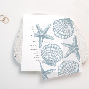 May include: A wedding invitation with a white background and blue starfish and seashell designs. The text on the invitation reads "Caroline & Justin Jacob".