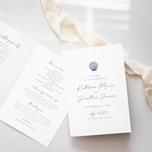 May include: Wedding invitation with a seashell design. The invitation is white with blue text and a seashell graphic. The text reads "Welcome to the wedding of Kathleen Marie and Jonathan James, September 26, 2026, Edge Hotel, Clearwater Beach, Florida."