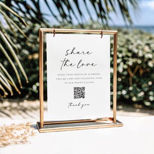 May include: A white sign with a gold frame, with the text "Share the love" and a QR code. The text below the QR code says "Share your photos by scanning this QR code and uploading them to our photo gallery." The sign also says "Thank you".
