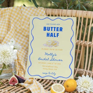 Può includere: Un invito per un addio al nubilato con il testo "SHE FOUND HER BUTTER HALF" in blu su sfondo giallo chiaro. L'invito è decorato con un bordo blu ondulato e include i dettagli per l'addio al nubilato di Molly. La scena comprende frutta e fiori.