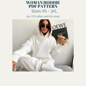 May include: White hoodie with a drawstring hood. The hoodie is shown on a model wearing white pants and sunglasses. The text "LOEWE" is visible in the background.
