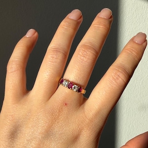 Peut inclure: Une bague en or avec une rangée alternée de trois rubis rouges taille ovale et deux diamants clairs taille ronde, disposés en ligne droite au centre de l'anneau pour former un design classique à cinq pierres avec une finition polie.