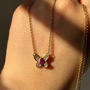 May include: A gold-colored butterfly pendant necklace with a ruby center stone and small clear stones on the wings. The delicate chain is also gold-colored.