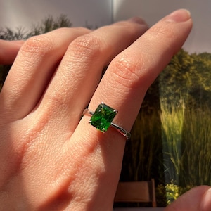 Puede incluir: Un anillo de plata con una gran piedra preciosa cuadrada de color verde esmeralda.