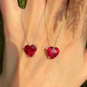 May include: Two heart-shaped necklaces with red gemstone pendants. One necklace has a silver chain and the other has a gold chain.