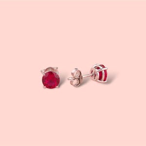 May include: A pair of silver stud earrings with a red gemstone in the center of each earring.