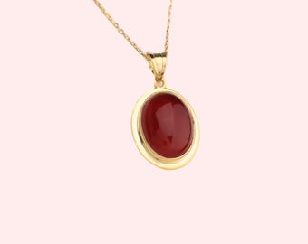 May include: A gold chain necklace with a pendant featuring a red oval gemstone set in a gold frame.