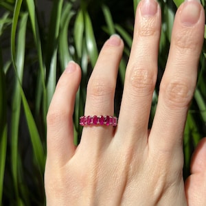May include: A gold band ring with a row of oval-shaped ruby gemstones.