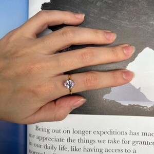 May include: A gold ring with a light pink oval-shaped gemstone. The ring is on a finger.