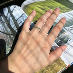 May include: A delicate gold band ring with a row of small, emerald green gemstones.