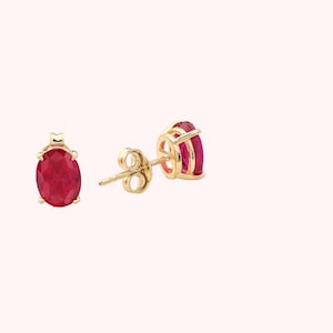 May include: A pair of gold earrings with oval-shaped red gemstones.