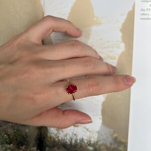 May include: A gold ring with a large, oval-shaped, red gemstone. The ring is on a person's finger.