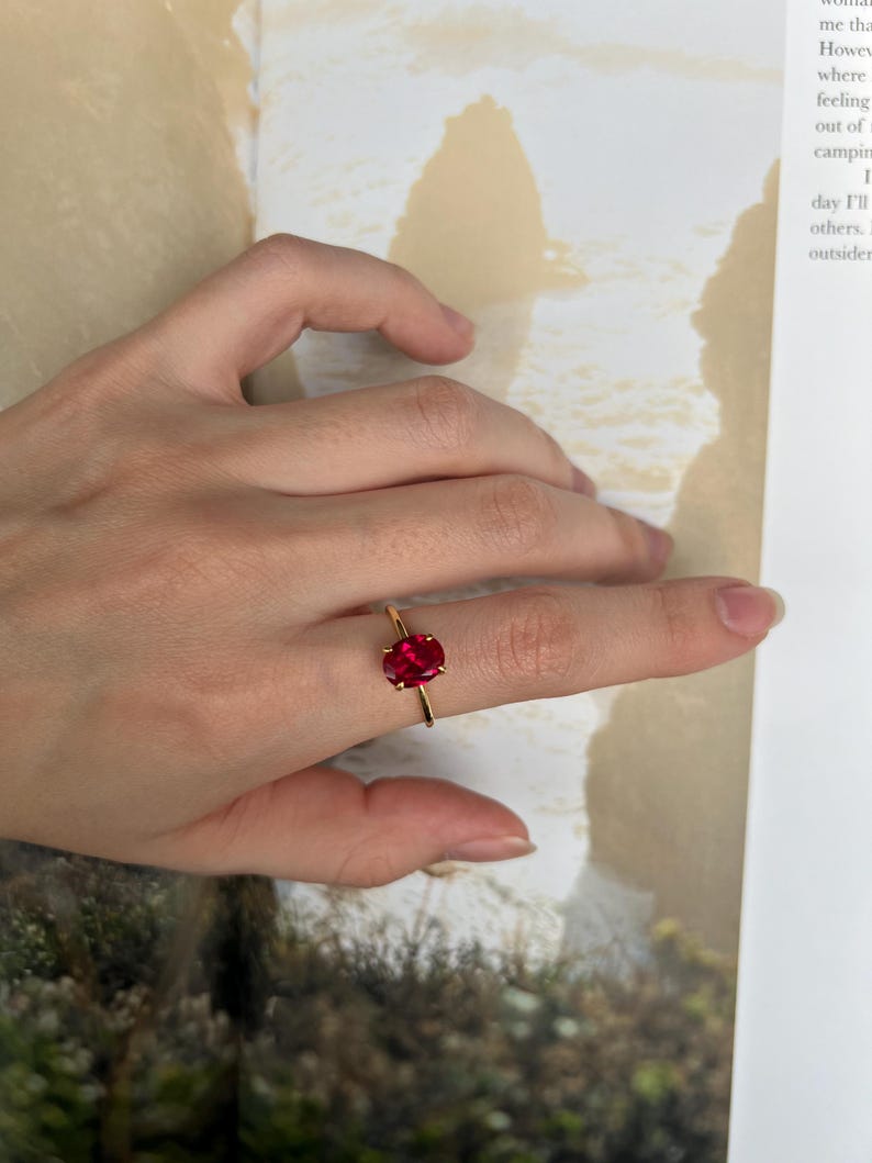 May include: A gold ring with a large, oval-shaped, red gemstone. The ring is on a person's finger.