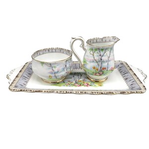 May include: A white porcelain tea set with a floral pattern on a white tray. The set includes a creamer and a sugar bowl. The tray has a scalloped edge and a gray and gold trim.