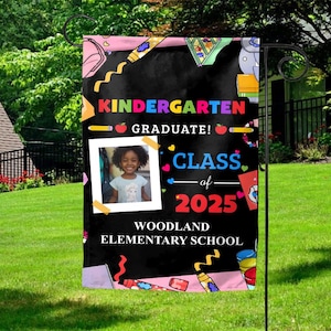 May include: A black and pink garden flag with a chalkboard design. It says "Kindergarten Graduate! Class of 2025" and has a photo of a young girl. The flag also has colorful illustrations of school supplies and the words "Woodland Elementary School".