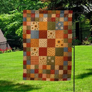 May include: A rectangular garden flag featuring a patchwork design of various fabric squares in autumn colors including orange, yellow, brown, green, and blue. The pattern includes floral prints with sunflowers and daisies, plaid, and solid textures.