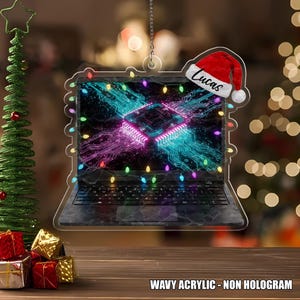May include: A clear acrylic laptop ornament with a colorful circuit board design on the screen. The ornament is decorated with string lights and a Santa hat with the name "Lucas". The text "WAVY ACRYLIC - NON HOLOGRAM" is at the bottom.