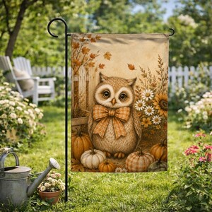 May include: A rectangular garden flag featuring a central illustration of a brown owl wearing a plaid orange and white bow tie. The owl is surrounded by orange pumpkins, white daisies, and autumn leaves against a light tan background.