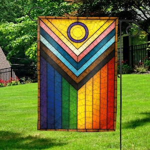 May include: A colorful garden flag with a stained-glass design. The flag features a yellow circle with a purple ring at the top, with a chevron pattern of various colors below. The bottom half is a vertical rainbow pattern.
