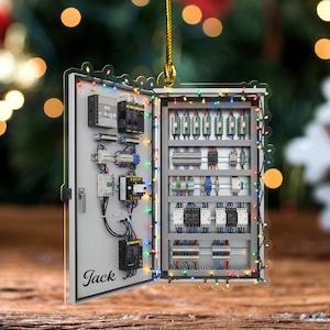 May include: A personalized Christmas ornament shaped like an electrical panel, with the name "Jack" printed on it. The panel is open, revealing detailed wiring and components, and is decorated with colorful string lights.
