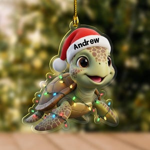 May include: A Christmas ornament featuring a cartoon turtle wearing a Santa hat with the name "Andrew" on it. The turtle is decorated with colorful Christmas lights and has a smiling expression. The ornament is hanging from a gold string.