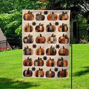 May include: A rectangular garden flag featuring a repeating grid pattern of quilted pumpkins in shades of orange, black, and cream. Each pumpkin is constructed from various fabric patches, accented by small black stars between the rows.