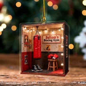 May include: A miniature boxing gym ornament featuring a red punching bag, boxing gloves, and a pair of black boots. The sign reads "Julian's Boxing Gym". The ornament is decorated with string lights and boxing posters.