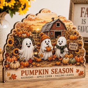 May include: A decorative wooden sign featuring a fall scene with three white ghosts, a red barn, sunflowers, and pumpkins. The text reads PUMPKIN SEASON, HAYRIDES, APPLE CIDER, FALLING LEAVES, and PUMPKIN PATCH. The sign has a scalloped top edge.
