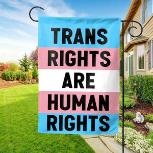 May include: A blue, pink, and white garden flag with the text "Trans Rights Are Human Rights" in black.