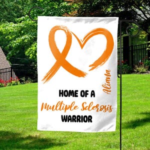 May include: White garden flag with an orange ribbon heart design and the text "HOME OF A Multiple Sclerosis WARRIOR". The name "Aliana" is printed vertically on the right side of the flag.