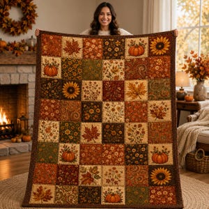 May include: A rectangular patchwork quilt featuring a repeating grid of squares with autumn-themed patterns, including orange pumpkins, yellow sunflowers, and brown maple leaves in shades of rust, gold, olive green, and deep brown with a dark border.
