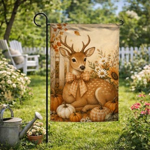 May include: A rectangular garden flag featuring a central illustration of a brown deer with a plaid bow tie, surrounded by orange pumpkins, white daisies, and sunflowers against a light tan background with a wooden fence motif.