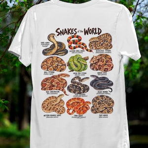 May include: A white t-shirt featuring a graphic print titled Snakes of the World. The design displays twelve detailed illustrations of various snake species, including a King Cobra, Ball Python, and Black Mamba, each labelled with its common and scientific name.