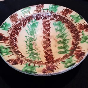 May include: A large, white ceramic bowl with a green and brown glaze. The glaze is applied in a swirling pattern, creating a unique and rustic look.
