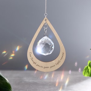 Puede incluir: Un atrapasol de cristal en forma de lágrima de madera con la inscripción "Aunque te hayas ido, tu luz permanece".
