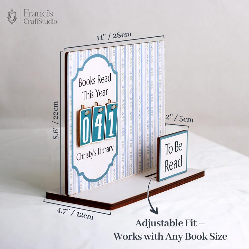 May include: A wooden book display with a white base and a blue and white patterned backdrop. It features the text "Books Read This Year" and "Christy's Library", with the number "041" displayed. The display is 11 inches wide and 8.6 inches tall.