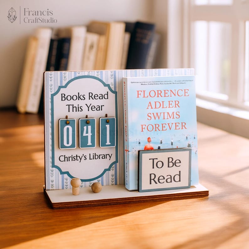 May include: A wooden book display with a counter showing "041" books read. The display includes a book titled "Florence Adler Swims Forever" and a "To Be Read" sign. The text "Books Read This Year" and "Christy's Library" are also visible.