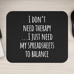 May include: Black rectangular mousepad with the text "I DON'T NEED THERAPY... I JUST NEED MY SPREADSHEETS TO BALANCE" in white. A black computer mouse and keyboard are visible.