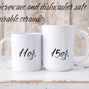 Op de afbeelding: Twee witte keramische mokken met zwarte letters. De kleinere mok heeft de tekst "11oz." en de grotere mok "15oz."