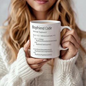 May include: White ceramic mug with a black graphic of code that reads "Boyfriend Code" with the text "#include "boyfriend.h"" and a code block with the text "for (i = 0; i < nAnniversaryCount; i++) { if (i == nToday) Boyfriend.RememberAnniversary(); else Boyfriend.FakeSurprise(); } if (Girlfriend NeedsAttention()) Boyfriend Give Compliments(): else Boyfriend. PlayVideoGames();".