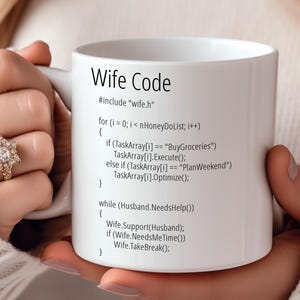 May include: White ceramic mug featuring a humorous code printed on it. The code is titled "Wife Code" and includes lines of code such as "#include "wife.h"" and "while (Husband.NeedsHelp())".