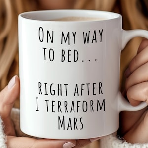 May include: White ceramic coffee mug with black text that reads "On my way to bed... Right after I terraform Mars".