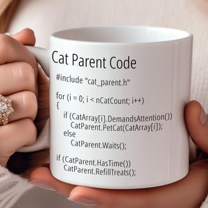 Pode incluir: Caneca de cerâmica branca com um design preto que diz "Cat Parent Code" e inclui um trecho de código engraçado. O código inclui o texto "#include "cat_parent.h"" e "CatParent.PetCat(CatArray[i]);".