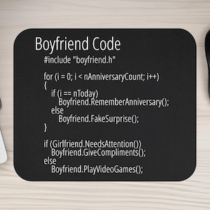 May include: Black rectangular mousepad with rounded corners. The mousepad features the text "Boyfriend Code" in white, followed by lines of code. A computer mouse and keyboard are visible in the background.